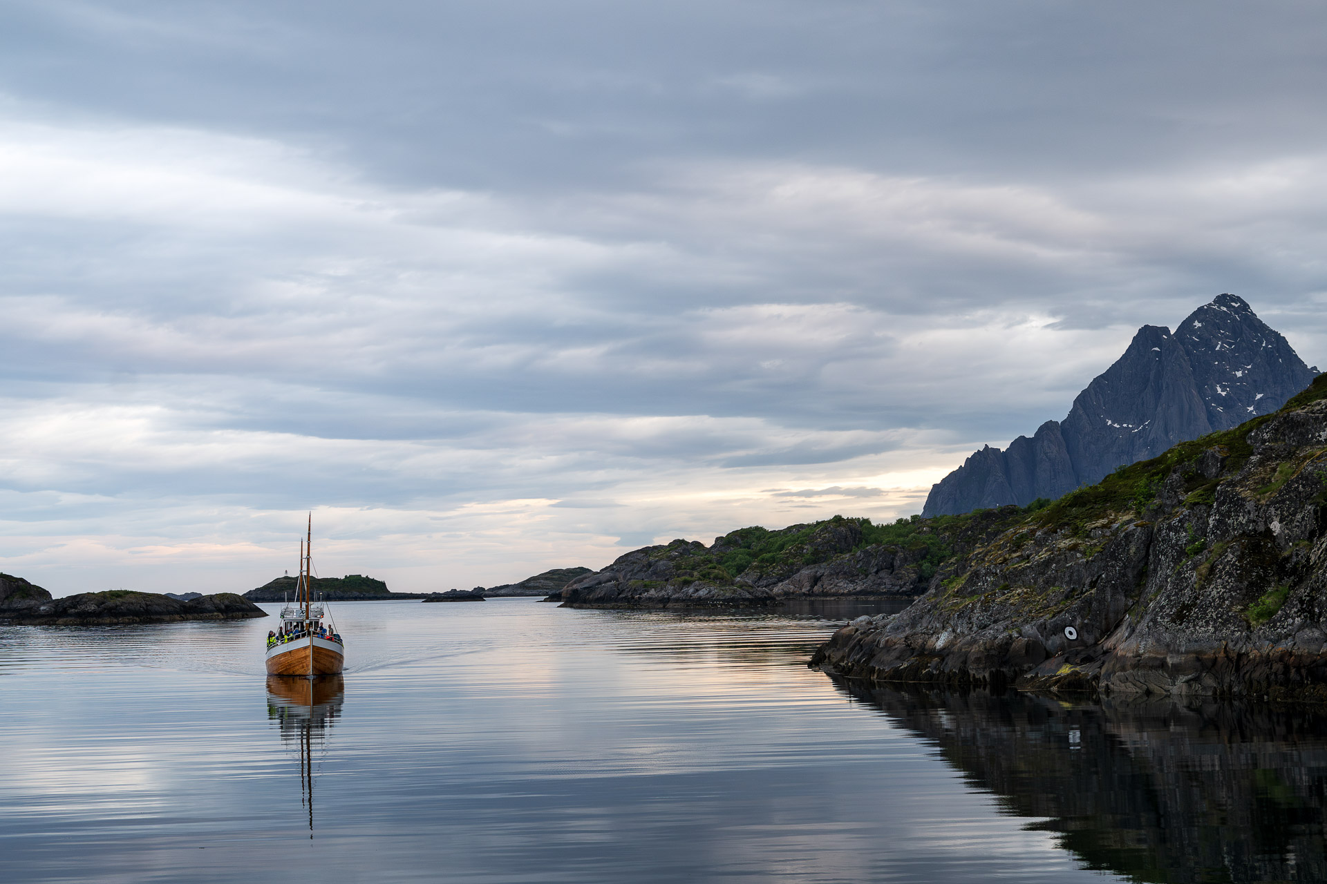Liten fiskebåt på stille fjord med fjell i Lofoten.